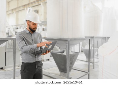 Industrial engineer wearing hardhat using laptop, controlling production process in modern flour mill