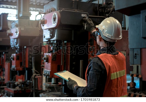 Industrial\
engineer worker wearing helmet and safe glasses, checking machinery\
and holding chart board, work at manufacturing plant factory,\
working with machine in industry\
concept