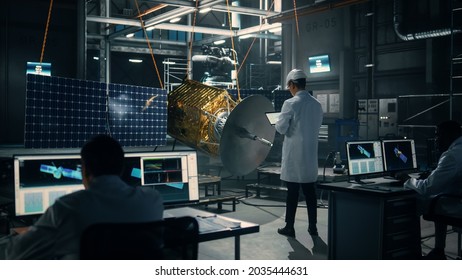 Industrial Engineer Working On Artificial Satellite Construction. Aerospace Agency: Scientist In Hard Hat Using Laptop Computer To Develop Spacecraft For Space Exploration And Data Communication.