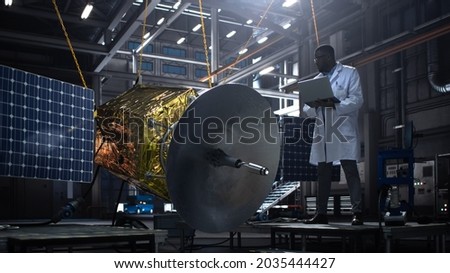 Industrial Engineer Working on Artificial Satellite Construction. Aerospace Agency: African American Scientist Using Tablet Computer to Develop Spacecraft for Space Exploration and Data Communication.