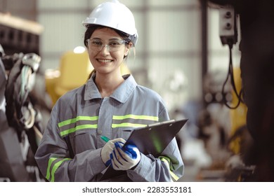 Industrial engineer working on robot maintenance in AI futuristic electronic technology factory. Female technician looking at camera checking automated robotic machine empowerment in industry 4.0.