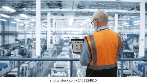 Industrial Engineer Working at a Technology Factory. Middle Aged Male Using Laptop Computer at Work, Browsing Electronics Information Online. Man's Back in Safety Vest Turned to Camera - Powered by Shutterstock