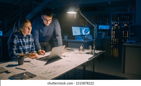 Industrial Engineering Facility: Female Engineer Working on Desktop Computer, Project Manager Stands Beside and Explains Specifics of the Task and Project Details. Working Late on Engine Prototype - Powered by Shutterstock