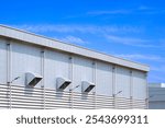 Industrial factory building with ventilation louver and rain gutter, rainwater drainage pipelines with LED solar wall lamps on aluminium wall against blue sky background, perspective side view 