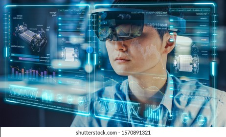 Industrial Factory Chief Engineer Wearing AR Headset Designs A Prototype Of An Electric Car Chassis On The Holographic Projection Blueprint. Futuristic Virtual Design Of Mixed Technology Application.