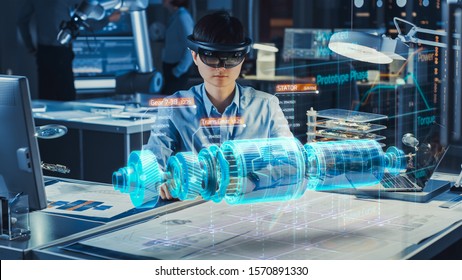 Industrial Factory Chief Engineer Wearing AR Headset Designs a Prototype of an Electric Motor on the Holographic Projection Blueprint. Futuristic Virtual Design of Mixed Technology Application. - Shutterstock ID 1570891330