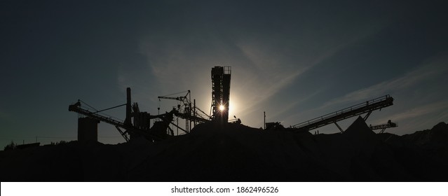 Industrial factory equipment, silhouettes of metal structures against the background of the evening sky and the setting sun, panorama. Mining industry.