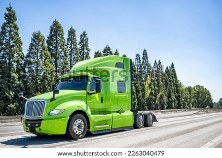Industrial grade professional use bright green powerful big rig semi truck tractor without the semi trailer running on the wide highway road to warehouse for picking up the next freight load