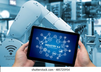 Industrial Internet Of Things Concept .Man Hand Holding Tablet With Infographic Industry4.0 Icons Screen And Blue Tone Of Automate Wireless Robot Arm In Smart Factory Background