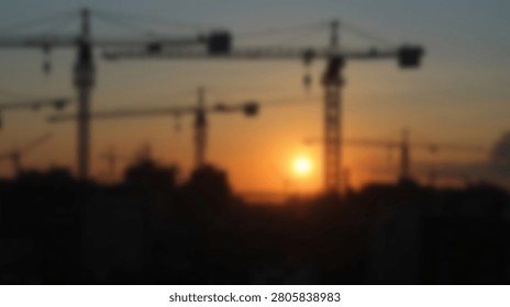 Industrial landscape featuring multiple tower cranes silhouetted against a bright setting sun and hazy orange horizon.