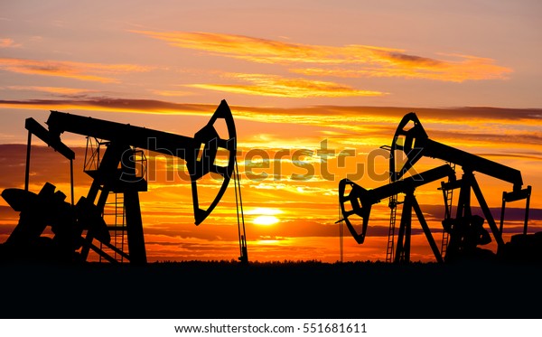 Industrial landscape. Oil Field. Oil pumps against\
the setting sun.
