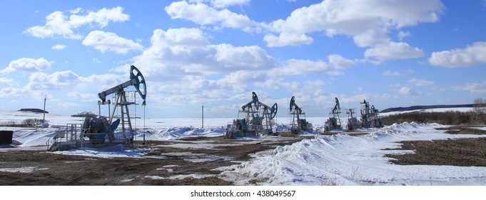industrial landscape Oil pumps in the field on a background of blue sky and white clouds on a sunny day in early spring