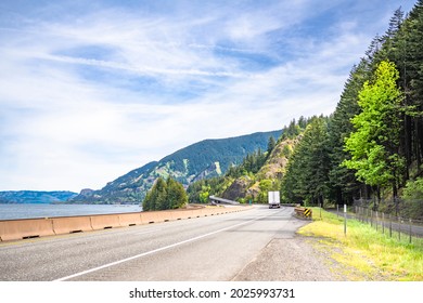 Industrial long hauler big rig white semi truck tractor transporting commercial cargo in dry van semi trailer running on the winding highway road along the Columbia river in Columbia Gorge area - Shutterstock ID 2025993731