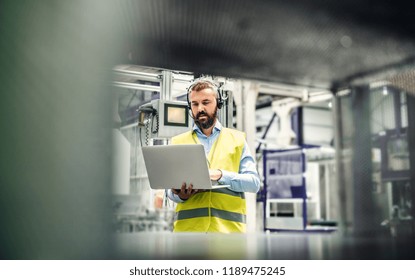 An Industrial Man Engineer With Headset And Laptop In A Factory, Working.