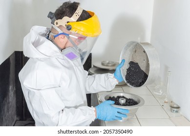 Industrial man worker in white protective overalls goggles, mask and face shield in an asphalt laboratory