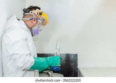 Industrial man worker in white protective overalls goggles, mask and face shield holding a test tube in an asphalt testing laboratory