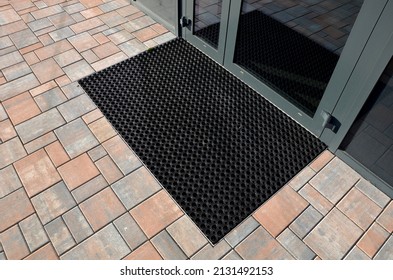 industrial mat cleaning zones at the entrance to the building. A black plastic-metal mat in the shape of an arch or half-circle lies on the limestone mosaic tiles - Shutterstock ID 2131492153
