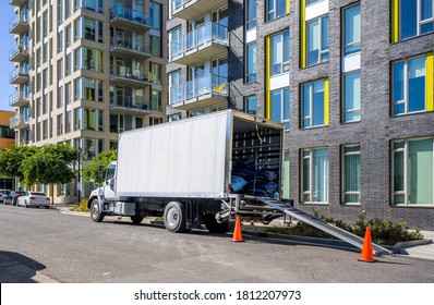 Industrial Medium-sized professional Big rig day cab semi truck with box trailer unloading delivered cargo standing on the urban city street with multilevel residential apartment buildings