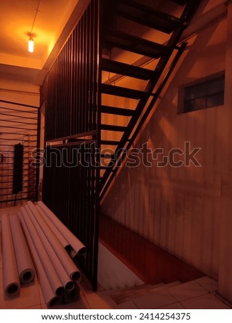 Industrial mezzanine stairways for employees' daily activities at work.The best shadows are created in the space by the yellow lighting, and the sturdy black metal steps look fantastic with white wall