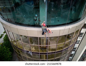 Industrial Mountaineering Worker Cleaning Window Of High-rise Building While Colleague Standing Behind Glass. Man Cleaner Using Safety Equipment While Washing Skyscraper Facade.