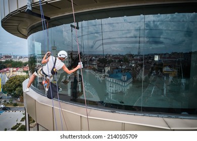 Industrial Mountaineering Worker Cleaning Window Of High-rise Building While Colleague Standing Behind Glass. Man Window Cleaner Using Safety Lifting Equipment While Washing Skyscraper Facade.