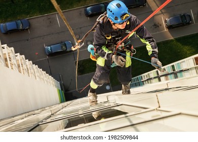 Industrial mountaineering worker hangs over residential facade building while washing exterior facade glazing. Rope access laborer hangs on wall of house. Concept of urban works. Copy space for site