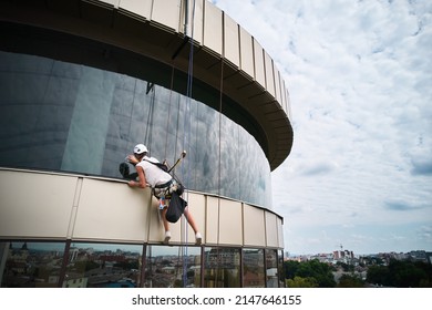 Industrial Mountaineering Worker Professional Cleaner Hanging On Climbing Rope And Cleaning Window Of High-rise Building. Man Window Washer Washing Skyscraper Facade.