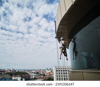 Industrial Mountaineering Worker Professional Window Washer Cleaning Glass Window Of Skyscraper. Male Cleaner Hanging On Climbing Rope While Washing Window Of High-rise Building.