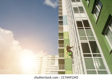 Industrial mountaineering worker washing exterior facade glazing hangs over residential facade building while at blue sky background. Rope access laborer hangs on wall of house. Copy space