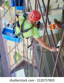 Industrial Mountaineering Worker Washing Glass Windows Of High-rise Building, Hanging On Safety Climbing Rope. Man Window Cleaner In Protective Helmet Cleaning Skyscraper Facade. Top View.