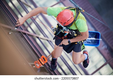 Industrial Mountaineering Worker Washing Glass Windows Of High-rise Building, Hanging On Safety Climbing Rope. Man Window Cleaner In Protective Helmet Cleaning Skyscraper Facade. Top View.