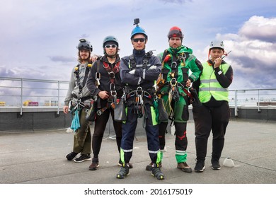 Industrial Mountaineering Workers In Uniform On Roof Residential Facade Building During High-rise Work. Rope Access Laborers On Roof Of House. Concept Of Industry Urban Works. Copy Space