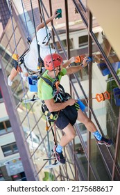 Industrial Mountaineering Workers Washing Glass Windows Of High-rise Building, Hanging On Safety Climbing Ropes. Men Window Cleaners In Protective Helmets Cleaning Skyscraper Facade. Top View.