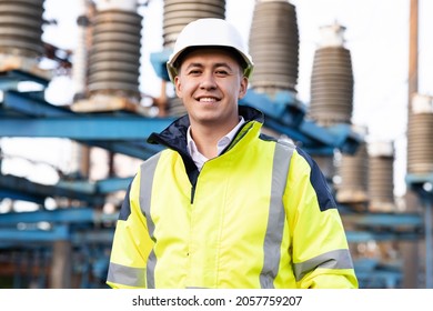 Industrial People. Sustainable Energy. Portrait Of Asian Ecology Worker In Hard Hat Standing At High Voltage Power Station. Technology