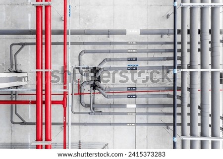 Industrial Piping on a Building's Ceiling, Overhead view of a complex network of industrial pipes and conduits installed along a building's concrete ceiling.