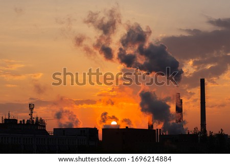 Industrial plant that works by burning coal with furnaces smoking abundantly at sunrise spreading thick clouds over the sky that polluting the  the environment.