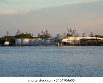 Industrial port with storage tanks and cranes against a twilight sky, reflected in the calm water - Powered by Shutterstock