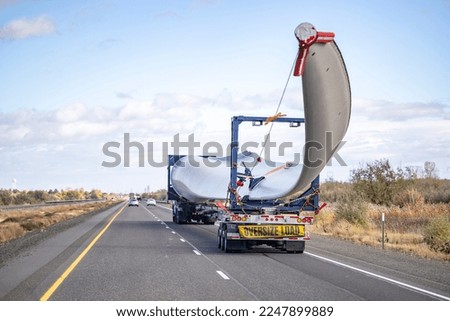 Industrial powerful big rig semi truck tractor with additional trolley transports oversize load a super long blade of a wind turbine with an escort car driving on the highway road in Columbia Gorge