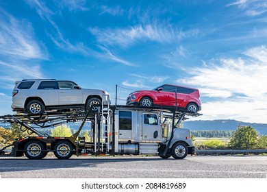 Industrial powerful white big rig car hauler semi truck transporting cars on two level modular semi trailer running on the winding road with dry grass and autumn forest on the hill in Columbia Gorge - Shutterstock ID 2084819689