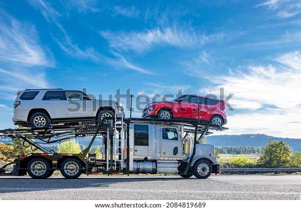 Industrial powerful white big rig car hauler semi\
truck transporting cars on two level modular semi trailer running\
on the winding road with dry grass and autumn forest on the hill\
\
in Columbia Gorge