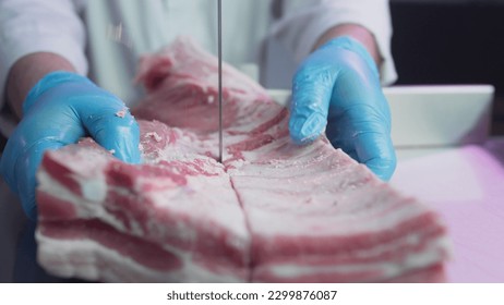 Industrial processing of meat. A man cook cuts a piece of tenderloin in a butcher's shop on a machine with a band saw. Ribeye or marbled beef. Ribs for restaurants, slaughterhouse. Slow motion, macro - Powered by Shutterstock