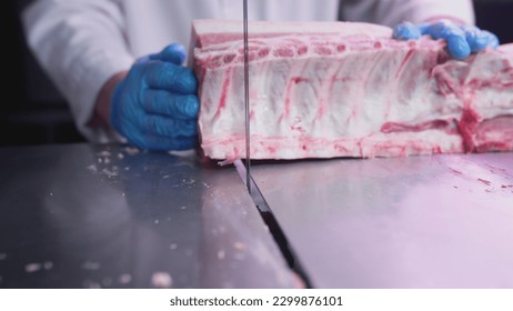 Industrial processing of meat. A man cook cuts a piece of tenderloin in a butcher's shop on a machine with a band saw. Ribeye or marbled beef. Ground meat production for restaurants, slaughterhouse - Powered by Shutterstock