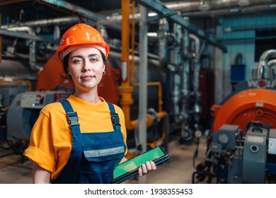 Industrial production concept. Portrait of a female engineer in uniform and helmet with a tablet in her hand. In the background-boiler equipment.