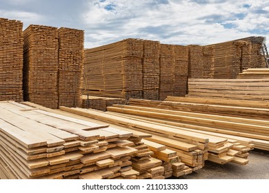 Industrial production of finished lumber products stacked in stacks on the warehouse territory. On an open background of blue sky with clouds.