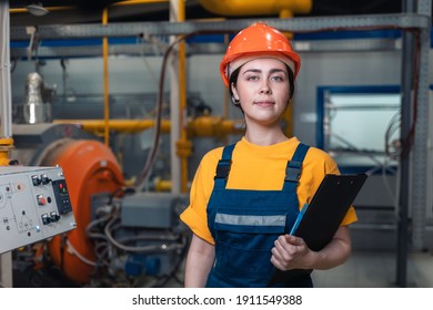 Industrial production. Portrait of a young Caucasian woman in uniform and helmet with a folder in her hand. In the background, boiler equipment. The concept of gender equality.