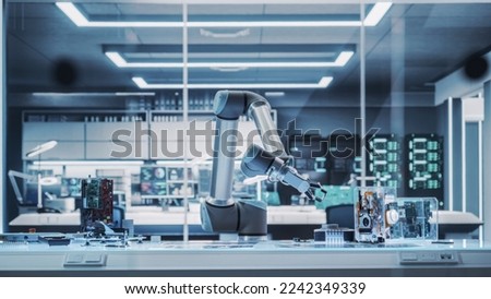 Industrial Programmable Robotic Arm in a Factory Development Workshop. Robot Arm Holding a Prototype Microchip. Tech Facility with Machines, Computers and Research Equipment. Photo Without People.
