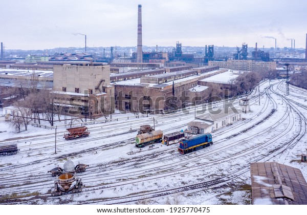 Industrial railway station in\
the snow against the backdrop of a metallurgical plant.  View from\
above.