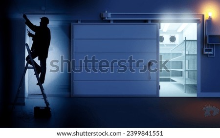 Industrial refrigerated warehouse. Man electrician on stepladders. Repair of freezing equipment. Silhouette worker. Gate to refrigerated warehouse open. Freezer equipment with empty shelves. 