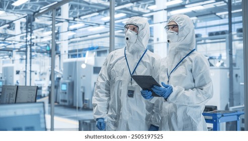 Industrial Scientists Wearing Disposable Protective Suits, Masks and Goggles at Production Plant. Specialist Using Tablet Computer, Analyzing Potential Work Hazards and Contamination at a Workplace - Powered by Shutterstock