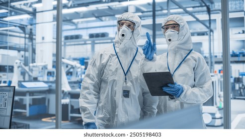 Industrial Scientists Wearing Disposable Protective Suits, Masks and Goggles at a Production Plant. Specialist Using Tablet Computer, Analyzing Potential Work Hazards and Contamination at a Workplace - Powered by Shutterstock